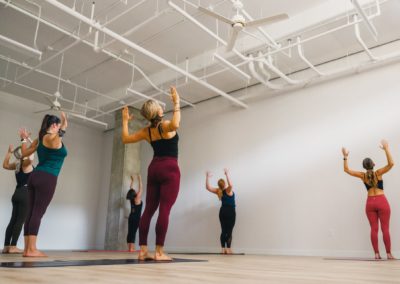 michelle young in green top and purple bottoms demonstrates a heart opener among 5 yogis on mats at my vinyasa practice in austin texas
