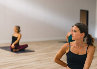 michelle young in green top and purple bottoms demonstrates a seated twist among 3 yogis on mats at my vinyasa practice in austin texas