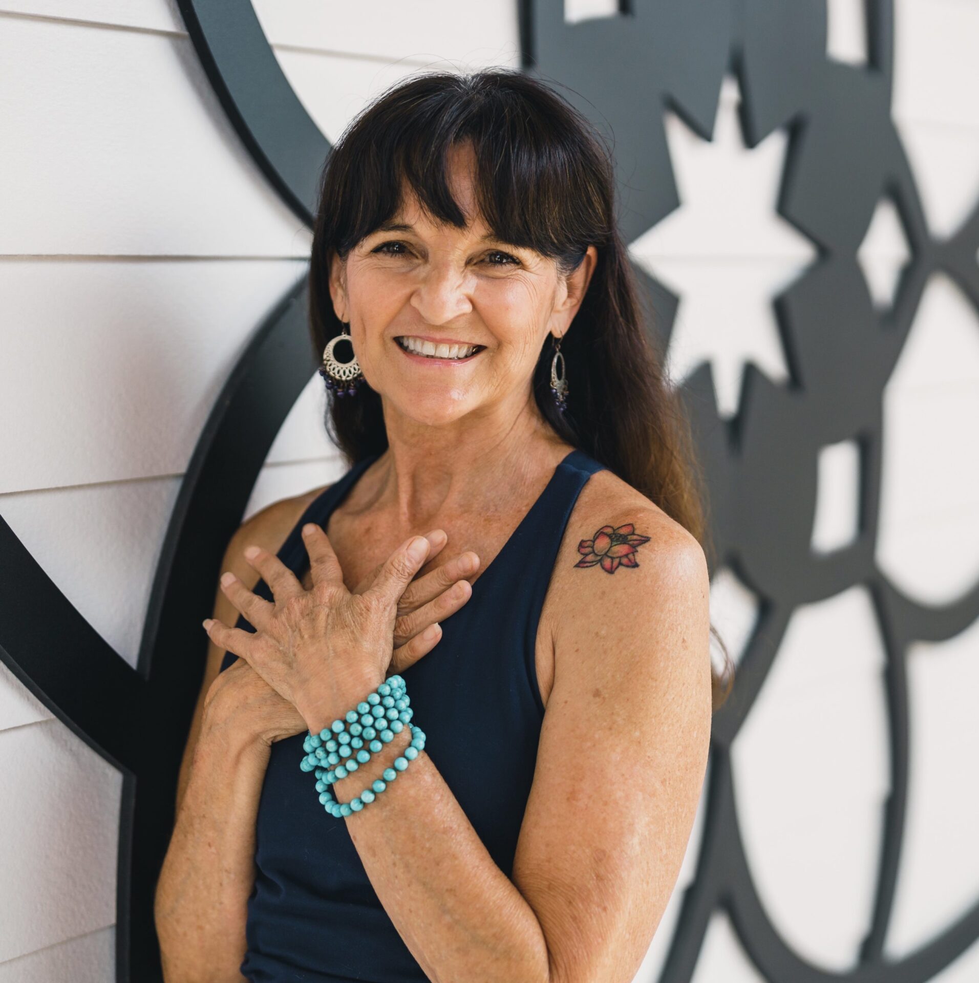 Leti Alvarez standing smiling with navy blue top and turquoise mala bracelet and hands crossed and pressed to her chest in front of the mandala at my vinyasa practice in austin texas