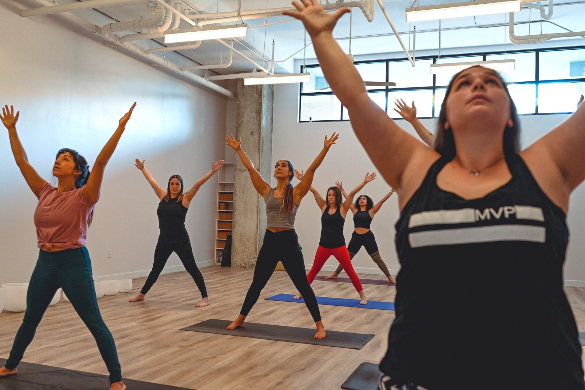 Michelle Young wearing a black top and black bottoms demonstrates star pose to 6 yogis standing on mats also practicing star pose at My Vinyasa Practice in Austin Texas
