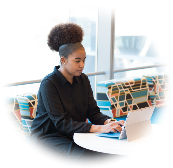 A woman sits in a work office on her computer. There is a window behind her.