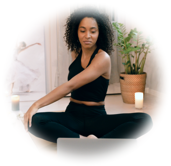 A woman sits on a yoga mat in front of her laptop.