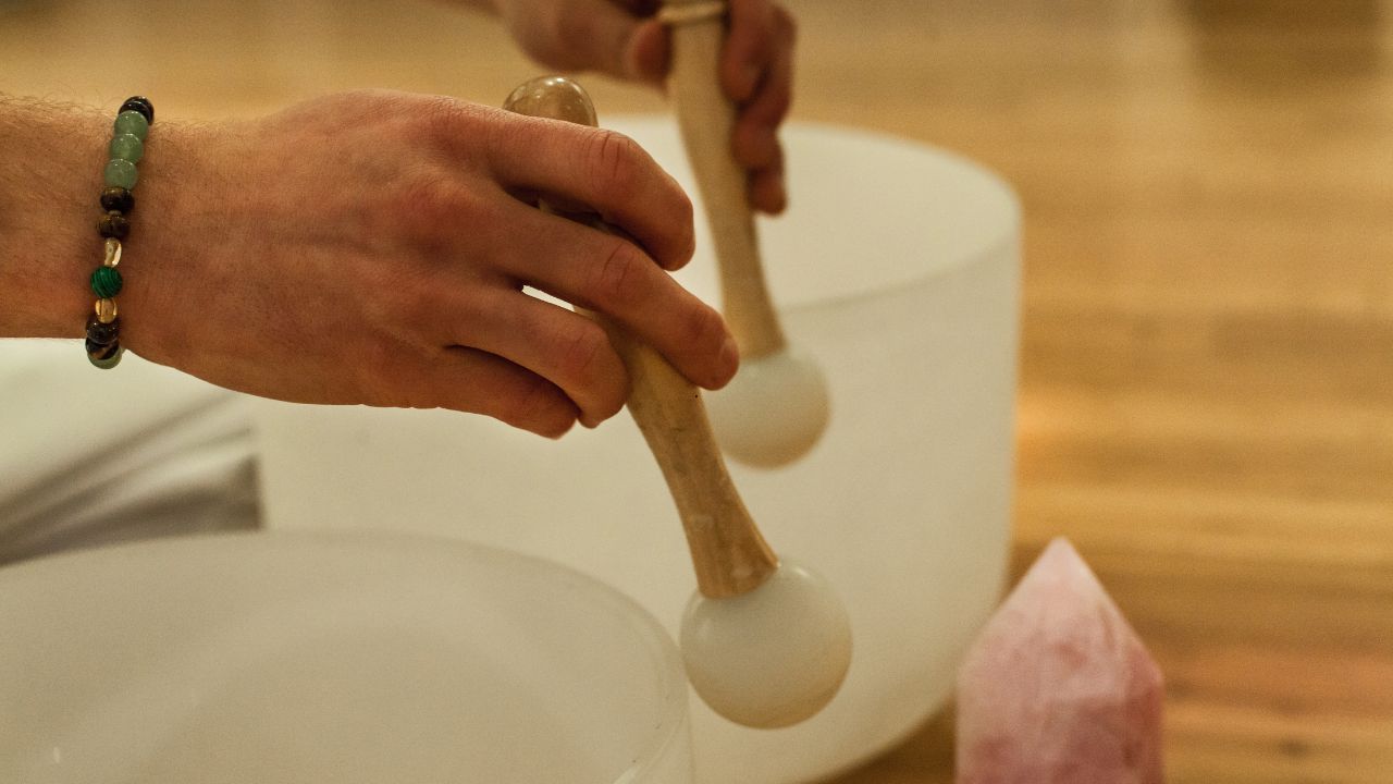 Ginger Bennett wearing a black top and black bottoms seated behind 6 singing bowls and in front of a large black and brass gong at My Vinyasa Practice in Austin, Texas, located near ACC's Highland Campus